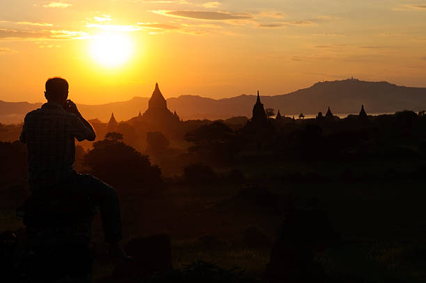 A man holds a camera to his face to photograph a spectacular sunset over centuries-old temples in Bagan, Myanmar (Burma)More of my images from Myanmar: