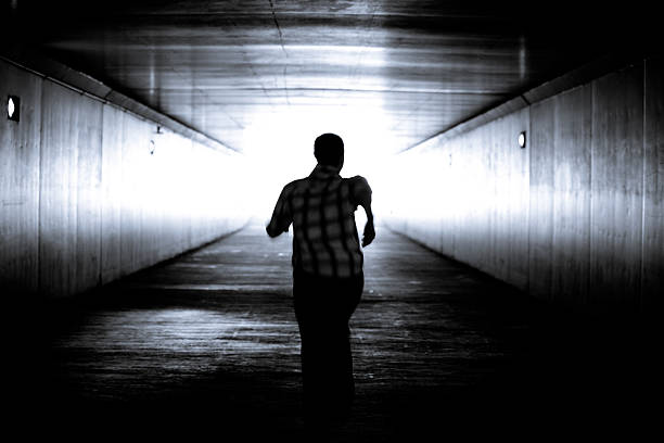 Balck and white image of man's silhouette running Black and white conceptual image.Man is running out of the tunnel into the light.  Motion blur. He is determined to get out of darkness into the light. There is hope and determination.    escaping stock pictures, royalty-free photos & images