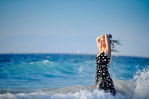 beautiful blond woman at seaside with arms raised feeling the waves.