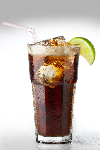 An ice cold soft drink of cola with a lime wedge and straw.