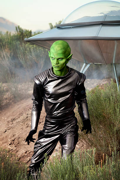 Green alien standing next to his UFO spaceship.