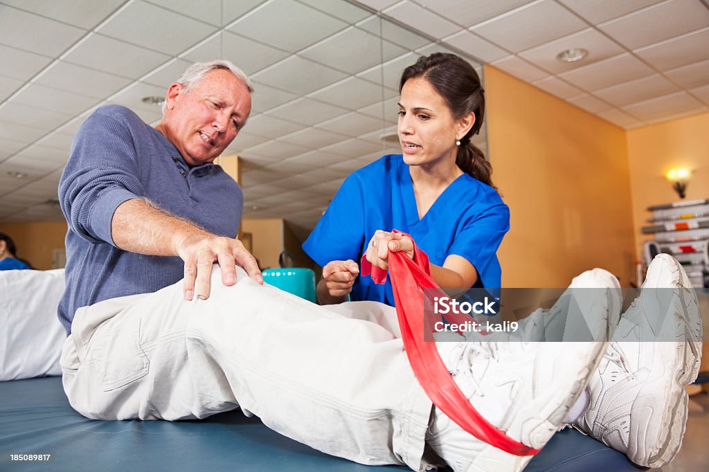 Physical therapist working with patient Physical therapist helping senior man (60s) with leg exercises.  Focus on knee. 20-29 Years Stock Photo