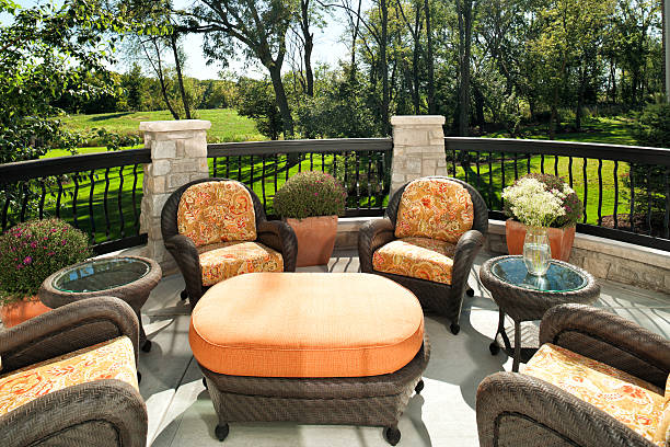 Wicker outdoor furniture decorates a homes lovely outdoor patio with a view over green summer wetland on a blue sky day.