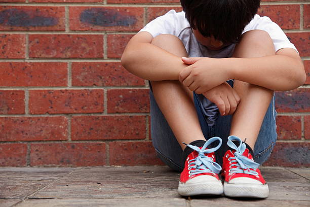 Tough Times Tough times. Concept for bullying or the challenges of growing up. Boy sitting with his head down against a brick wall. Copy space. one little boy stock pictures, royalty-free photos & images