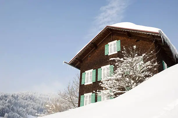 "Typical wooden house in a snowcovered landscape. Located in Riezlern, Kleinwalsertal in Austria. There are some snowflakes visible."