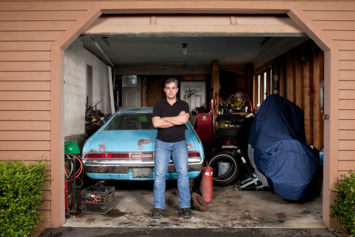 A man in his garage leaning against an old car.