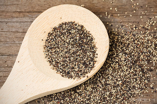 Black Pepper on Wooden Spoon Coarse ground black pepper on a wooden spoon and spilled on an old, weathered wood surface. black peppercorn stock pictures, royalty-free photos & images