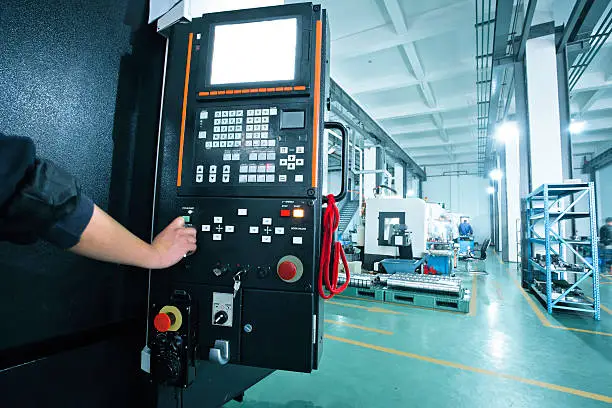 workers operating the controls of a CNC machine that manufactures parts for the aerospace Industry.