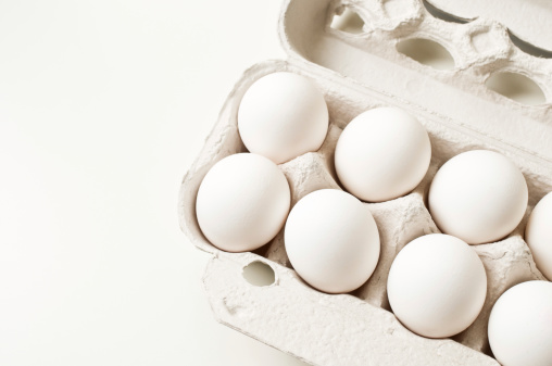 White eggs in carton on white background.