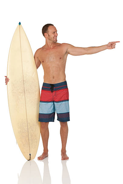 человек стоят с доски для серфинга и, указывающая на что-то, - swimming shorts surfing male full length стоковые фото и изображения