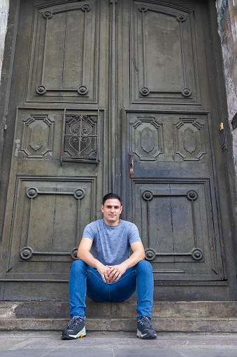 Portrait of a man sitting in a doorframe looking at the camera.