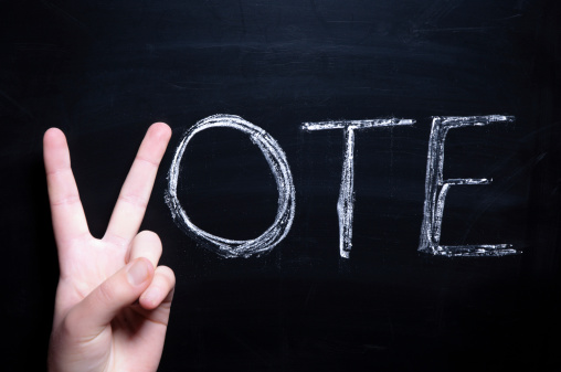 A stock photo of Vote on a blackboard with a human hand as the V