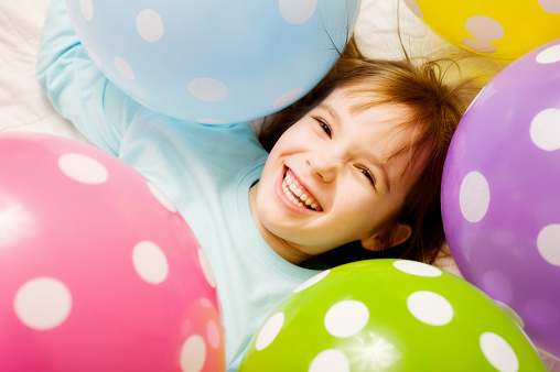A seven year old is surrounded by fun, brightly colored balloons.