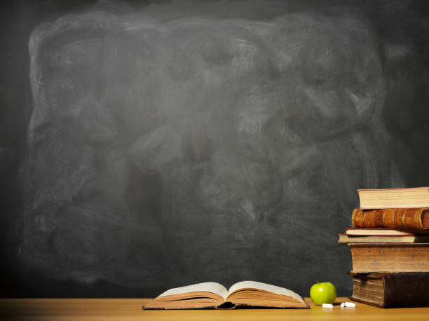 Vintage wood school desk with stack of teal and grey books and jar of pencils and pens with copy space and a black background