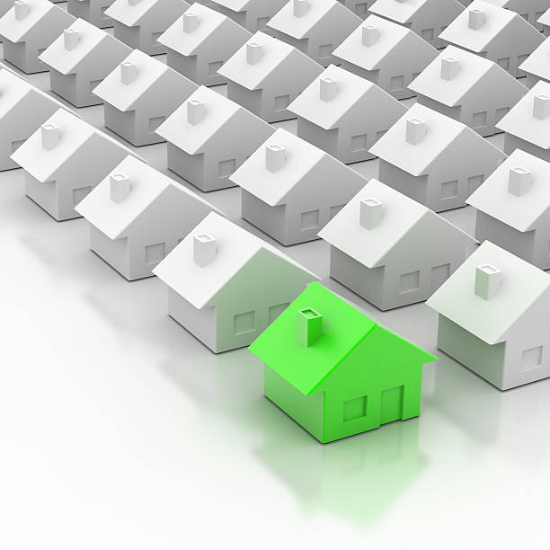One green miniature house in a group of ordinary white homes stock photo