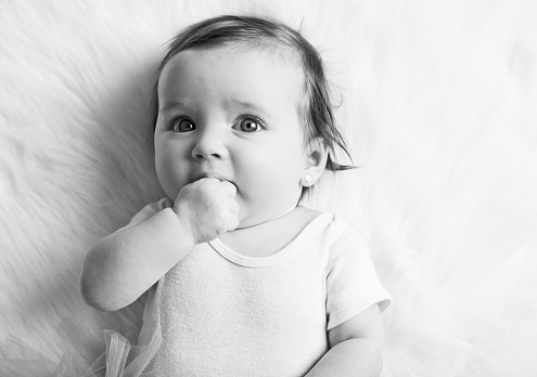 Black and white image image of a three month old baby girl smiling at the camera while laying down and wearing a tutu.