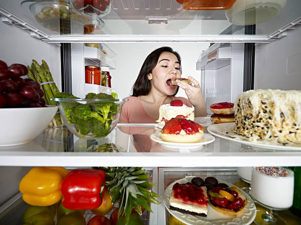 Young Woman Eating Donut Young woman eating donut from fridge. pepper cake stock pictures, royalty-free photos & images