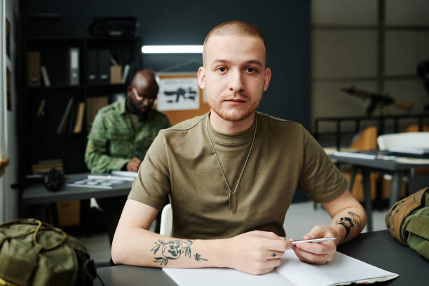 istock Young serious man in t-shirt looking at camera while sitting by desk 1851057851