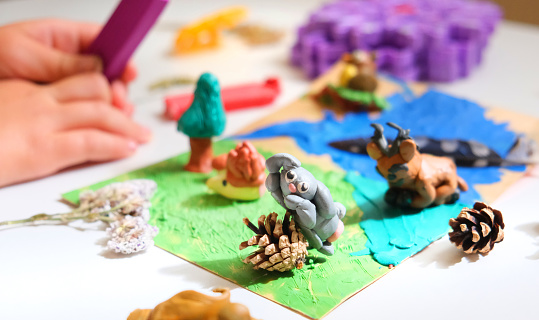 Child smearing colorful plasticine on cardboard and creating fairy tale card with cartoon animals