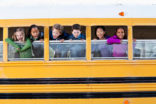 Multi-ethnic elementary school students (5 to 9 years) in school bus, looking out windows.
