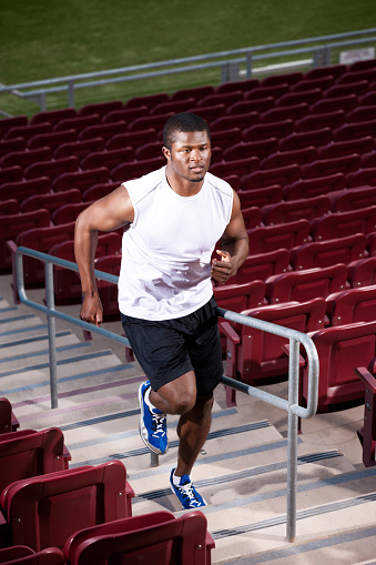 Action shot of a muscular african american male athlete training by running up the stairs of an empty sports stadium.