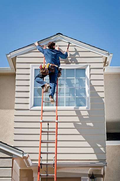 Handyman In Uniform Hammering Male caucasian handyman in uniform and tool belt, hammering the siding on the 2nd story window of a Cape Cod style house. clothing north america usa massachusetts stock pictures, royalty-free photos & images