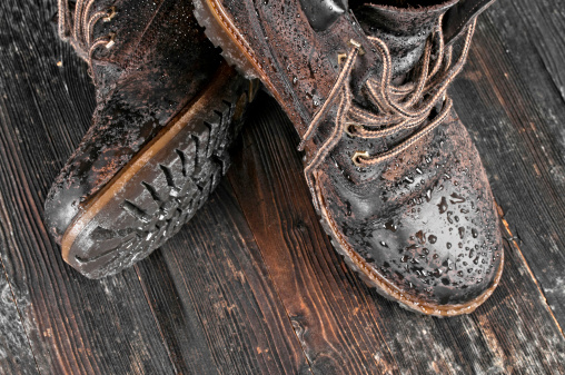 Brown wet hiking boot on wooden background