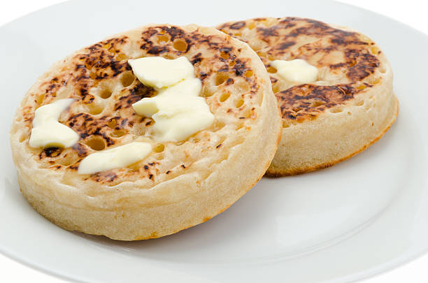 Stock photo showing an elevated view of a turquoise blue, plate containing a pile of freshly baked, warm, homemade crumpets.