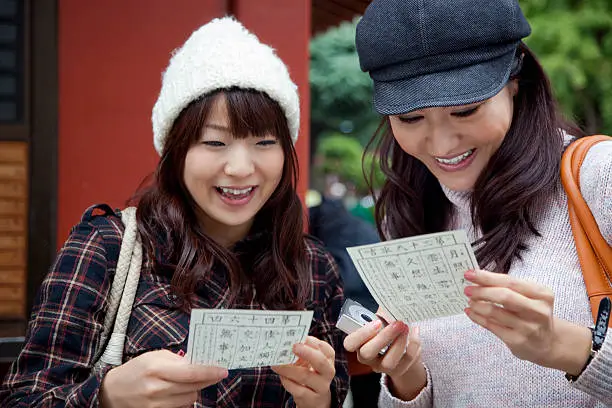 Two happy young Japanese women reading fortune papers omikuji (fortune paper) at Sensoji Temple in Asakusa, Tokyo. iStockalypse Tokyo, Japan. 