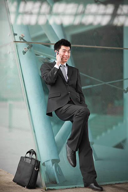 istock Chinese businessman using cellphone, leaning on glass wall 185110410