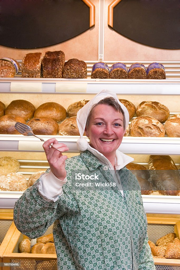 Female Bakery Shop Assistant Portrait of a smiling female bakery shop assistant with a pointed cap holding up a pastry tongs.Copy space on blackboards in background. Adult Stock Photo