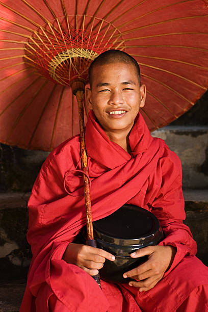 Young burmese buddhist monk novice looking serious against a teal wall