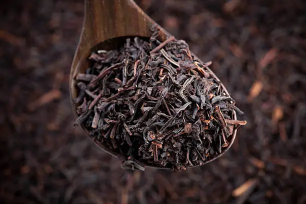 "wooden tea spoon full of black, Englisk breakfast tea leafs; closeup, blured tea background"