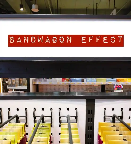 Photo of Store product shelf with tag written BANDWAGON EFFECT -  refers to psychological phenomenon tendency to adopt or follow trends or certain behaviors, styles or attitudes - doing something because others are doing so