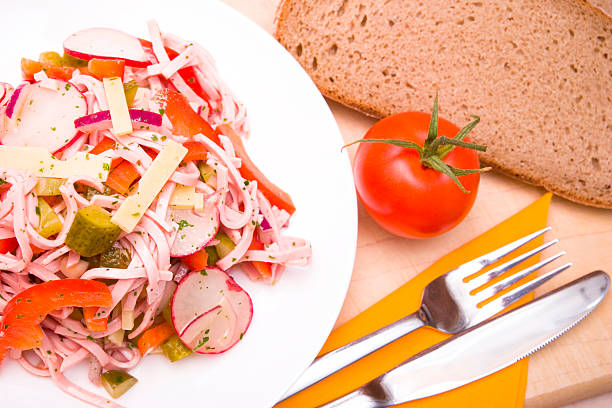 Close-up of a portion sausage salad on a plate served on a cutting board with bread.