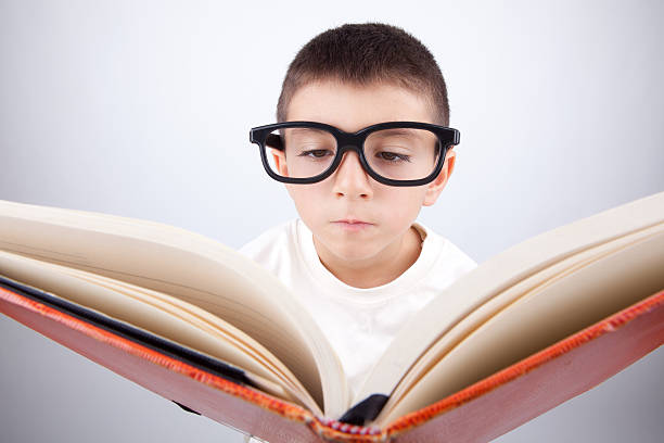 Nerd little boy with large glasses reading book