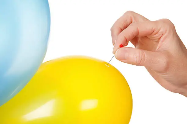 Close-up of a hand holding a needle to burst a balloon. Studio isolated on a white background.