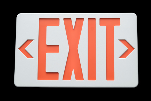 Close up of an Emergency Exit Sign against a black background.  See also
