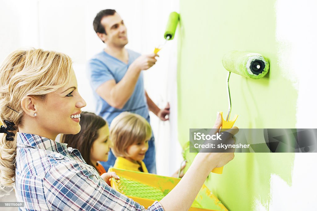 Happy family painting walls. Portrait of a happy family holding paint rollers and painting wall in green. Painting - Activity Stock Photo