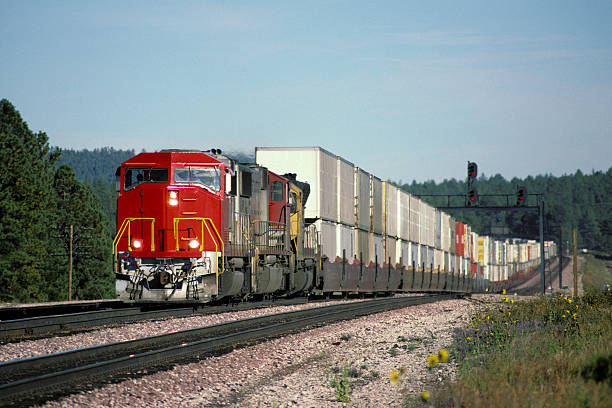 Red locomotive and double stack freight train A long double stack container train hauled by a bright red locomotive speeds eastward through a forest of conifers.  Headlights and ditch lights are on for safety.  Logos and trademarks removed.  Copy space. freight train stock pictures, royalty-free photos & images