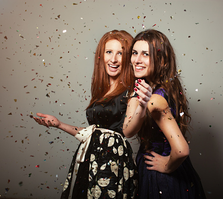 Two dressed up girls standing under confetti rain