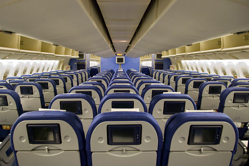 Airplane interior with rows of empty blue seats with video screens.