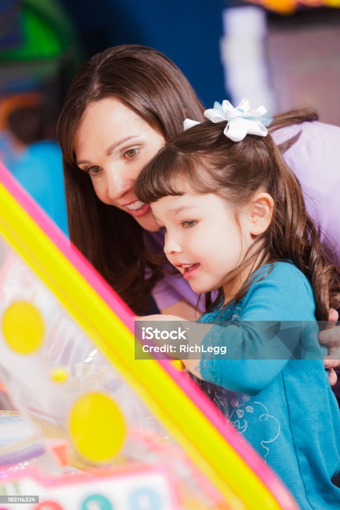 Mother and Daughter in an Amusement Arcade A mother helps her daughter play a game in an amusement arcade. Amusement Arcade Stock Photo