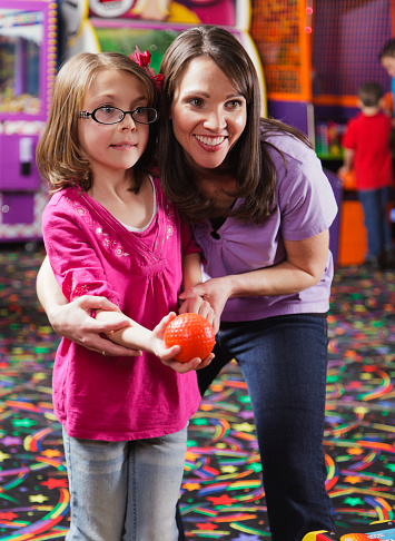 A mother helps her daughter play skeeball in an amusement arcade.