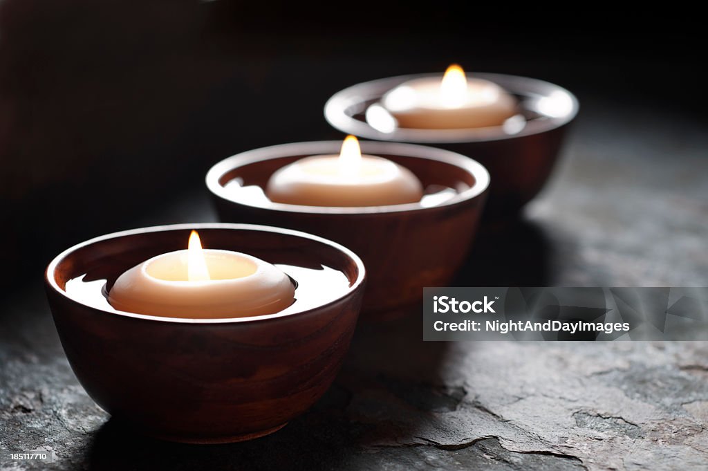 Three lit candles floating in wooden bowls filled with water SEVERAL MORE IN THIS SERIES. Floating candles on a slate surface in a low key, zen environment.  Very shallow DOF. Zen-like Stock Photo