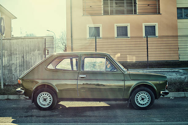 Retro green car with white roof parked on grass near a modern cafe entrance with plants and chalkboard menu, blending vintage charm with urban lifestyle
