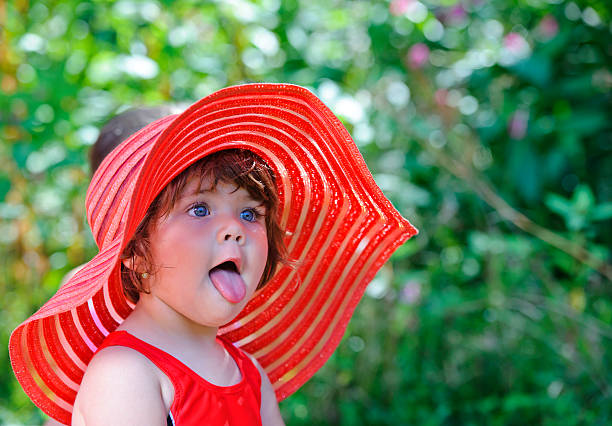 playful little girl sticking tongue out wearing red summer hat.