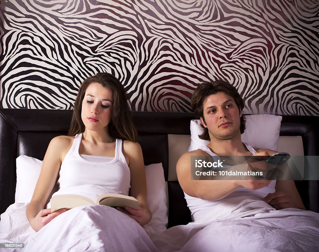 No Desire Young couple in bed.Husband watching tv while her wife reading book and they are not interested each other Bed - Furniture Stock Photo