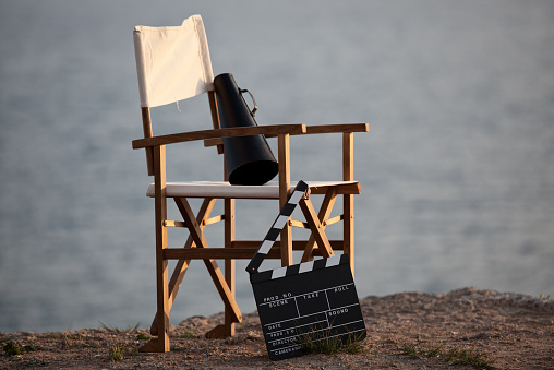 Director's chair in outdoor with megaphone and film slate.Fosuc is on the chair.Sea background is defocused.Horizontal composition.Shot with a full frame DSLR camera.