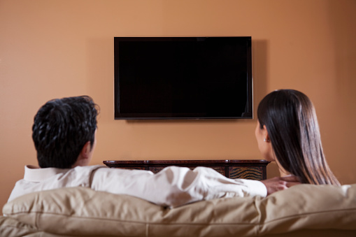 Rear view of Asian couple watching TV.  Focus on flat screen.